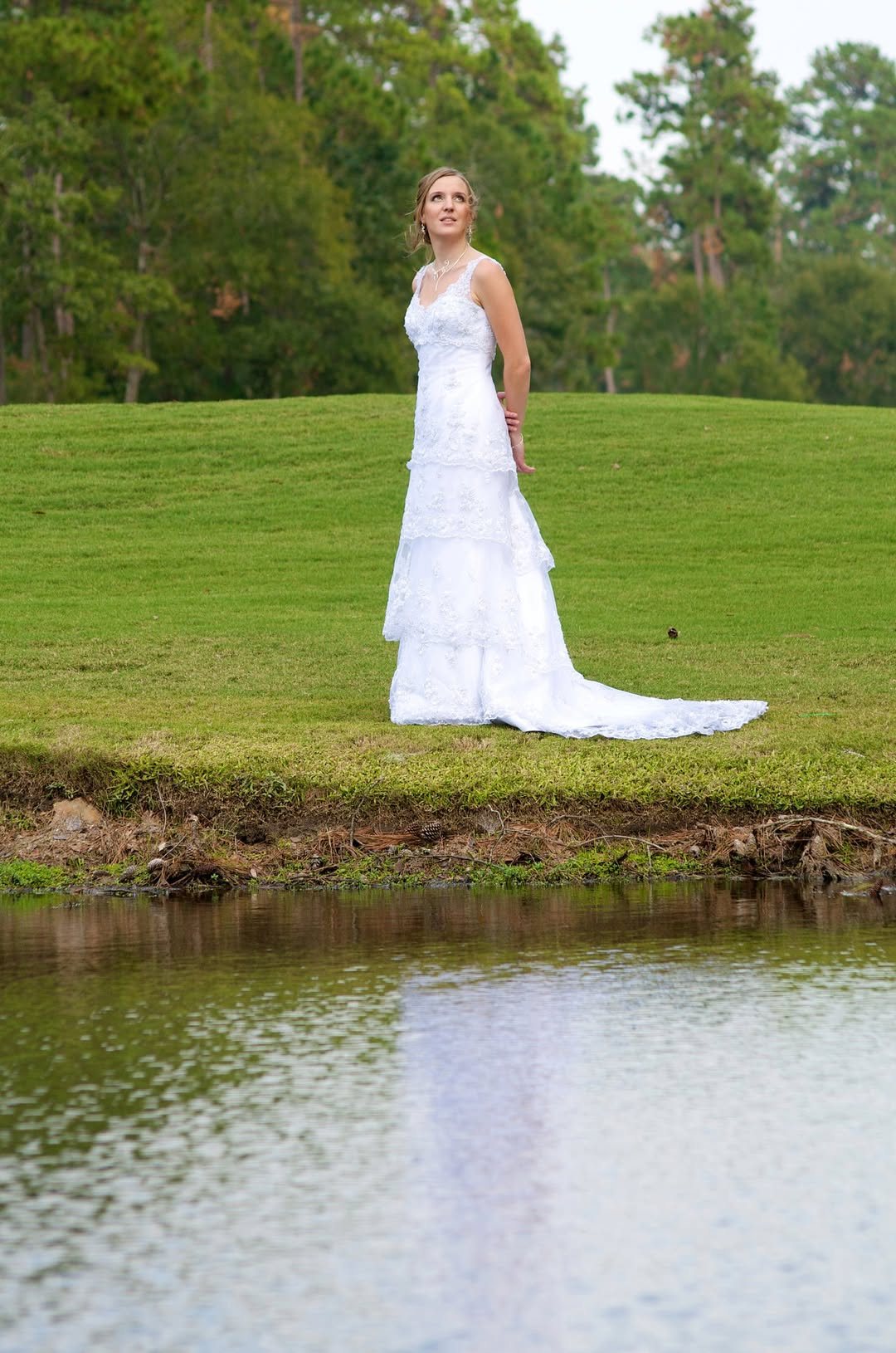 Bride standing on a grassy bank beside a pond