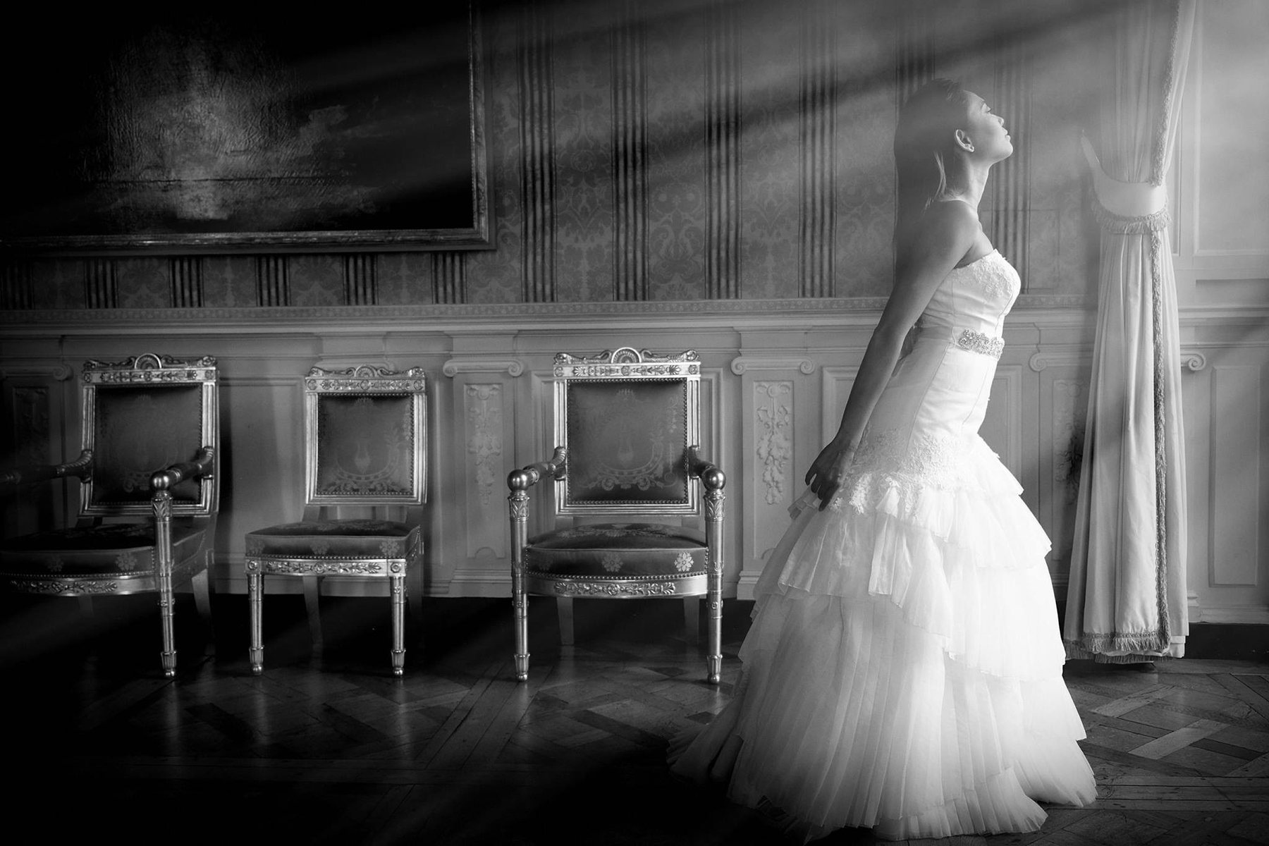 Black-and-white portrait of a bride standing in dramatic window light