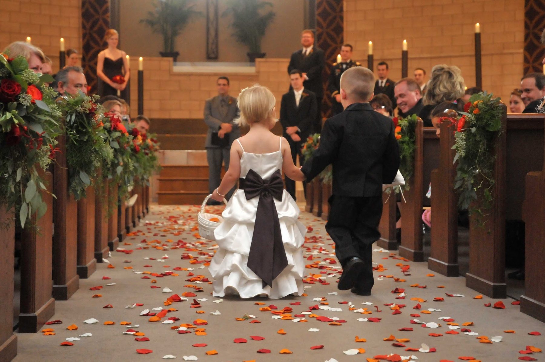Young wedding attendants walking down a flower-covered aisle