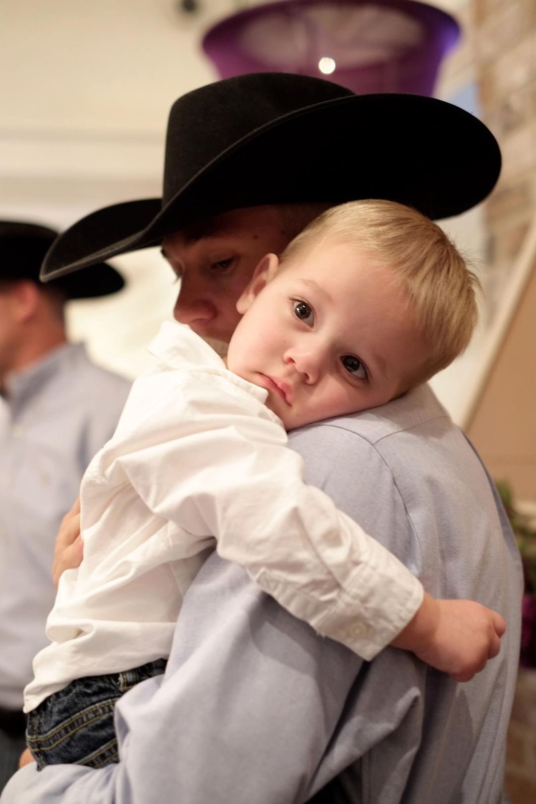 Young child resting on a father's shoulder at a wedding