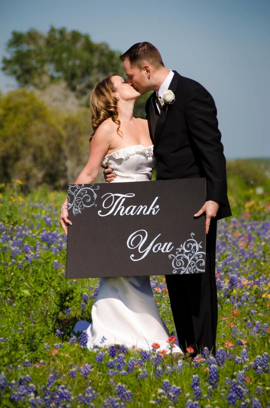 Newlyweds kissing in wildflowers while holding a thank-you sign